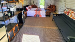 A tented accommodation with a bed, seating area, kitchenette, and a view through the entrance.