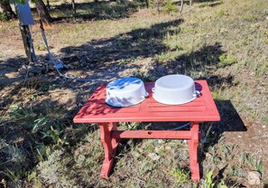 Uma mesa vermelha com dois objetos brancos, ao ar livre, com grama e pedras ao redor.