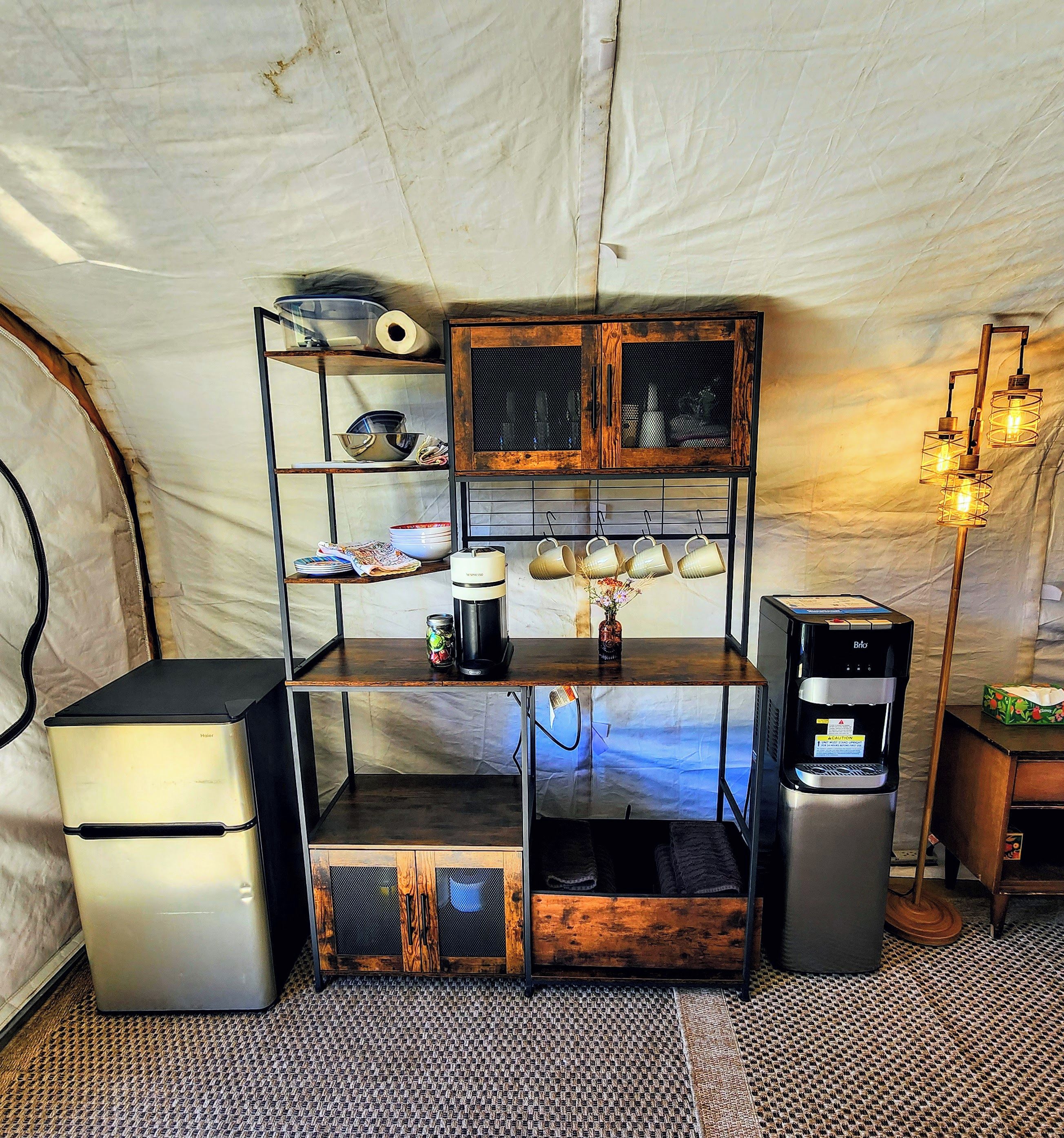 Una kitchenette compacta con cafetera, refrigerador pequeño y dispensador de agua.