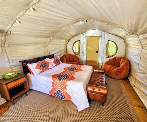 A tent with a bed, two chairs, a small table, and a door.