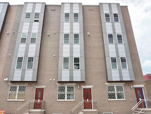 A multi-story building with a brick facade, large windows, and a series of doors and railings.