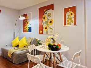 A cozy room with a sofa, a dining table with chairs, and artwork on the walls.