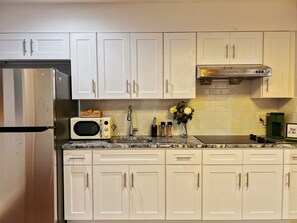 A kitchen with white cabinets, a stainless steel refrigerator, a microwave, a sink, and a coffee maker.