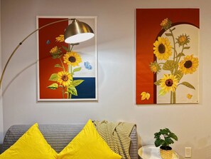 A room with a sofa, a lamp, and two framed artworks depicting sunflowers.