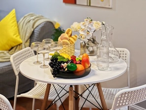 Una mesa redonda con un frutero, copas de vino y una jarrón.