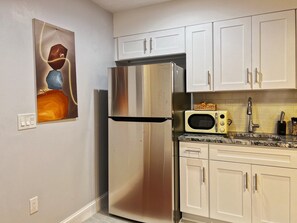 Une cuisine équipée d’un réfrigérateur en acier inoxydable, de meubles blancs, d’un four à micro-ondes et ornée d’un tableau au mur.