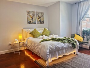 A neatly made bed with white linens and green floral throw blankets, a bedside table with a lamp, and two paintings of deer on the wall. - Ramblei near Chinatown & CenterCity: 2-Bedroom - Unit C (Philadelphia)