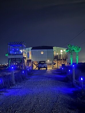 Un bâtiment moderne avec une voiture garée devant, un espace abrité sur la gauche et des palmiers sur la droite.