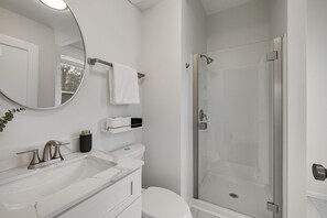 A modern bathroom with a white sink, a toilet, a glass shower enclosure, and a round mirror. - Walking distance to Historic Main Street, St. Charles, MO (Saint Charles)