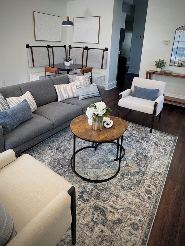 A modern living room with a grey sofa, a round coffee table with a vase, a white armchair, and a patterned rug. - Walking distance to Historic Main Street, St. Charles, MO (Saint Charles)