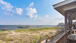 A wooden deck with a view of the beach and a pier extending into the water. - Beautiful bayfront home with views of the Dauphin Island Bridge (Dauphin Island)