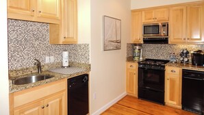 Una cocina con gabinetes de madera, encimera de granito, pileta de acero inoxidable, microondas, estufa y lavavajillas.