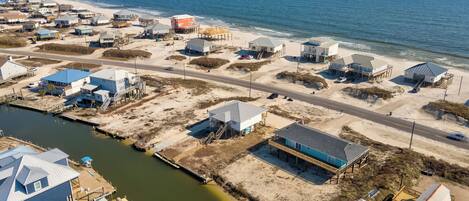 An aerial view of a coastal area with multiple buildings, a road, and a body of water.