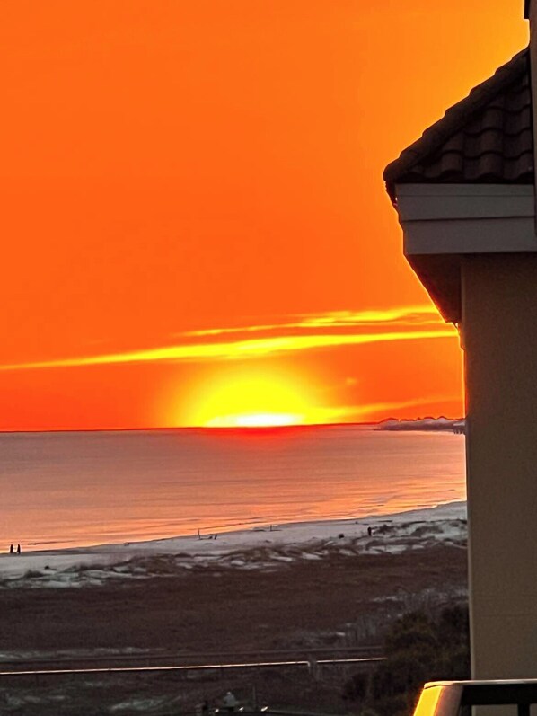 A sunset over a beach with a building in the foreground. - 7th Floor Penthouse Unit at Gulf Front Condo (Dauphin Island)