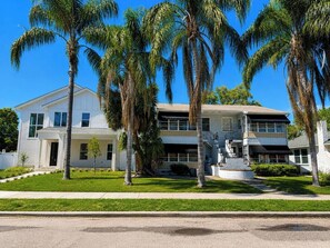 A two-story residential house with a front porch, palm trees, and a well-maintained lawn.