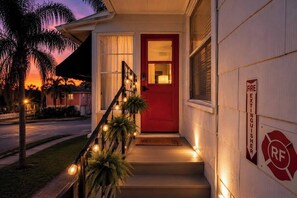 A house with a red door, a fire extinguisher sign, and a staircase with string lights.