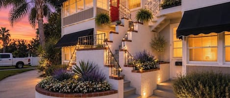 A two-story house with a red door, a staircase with string lights, and a white exterior.