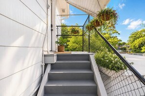 Una escalera conduce a un balcón con una cerca de malla metálica, plantas en macetas y una vista despejada del follaje circundante.
