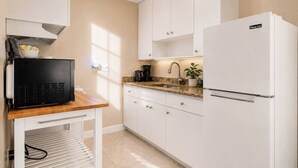 A modern kitchen with white cabinets, a black countertop, a white refrigerator, and a coffee maker.