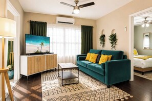 Ein Wohnzimmer mit einem salbeigreenen Sofa, einem Couchtisch, einem Fernseher und einem Deckenventilator.