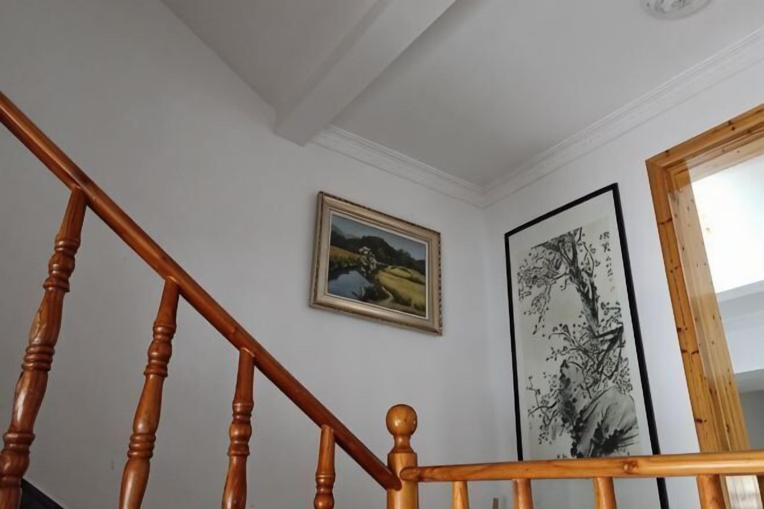 Una escalera con balaustres de madera, un cuadro con paisaje enmarco y una obra de arte vertical en la pared.