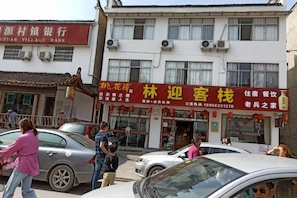 A building with a storefront featuring a sign with Chinese characters, a visible entrance, and parked cars in front. - Chaji Lin Ying Inn (Jing County)