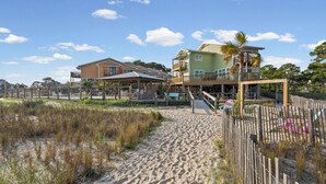 A beachfront property with a sandy walkway, wooden deck, and a two-story building with balconies.