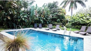 Piscina con sillones de descanso y un exuberante jardín tropical.