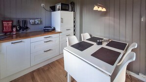 Et kompakt køkken med hvide skabe, en træbordplade og et spisebord med fire stole.
