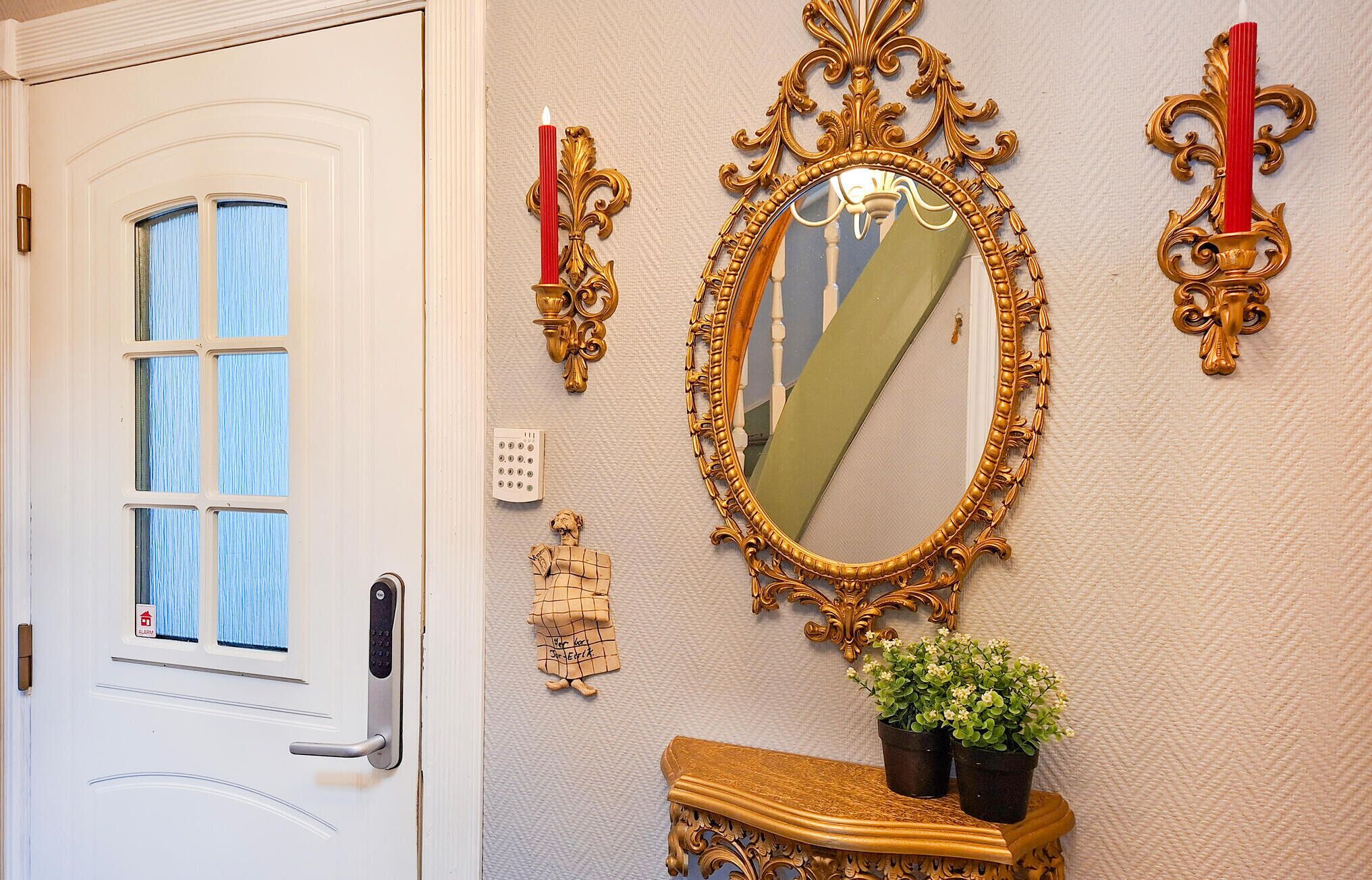 A door with a window, a wall-mounted ornate mirror, a wall clock, a small statue, and a potted plant on a console table.