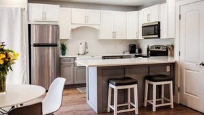 Une cuisine moderne avec des meubles blancs, un réfrigérateur en acier inoxydable, un four à micro-ondes et un coin bar équipé de tabourets.