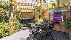 Een terras buiten met een houten pergola, een tafel met stoelen, een barbecue en een kleurrijke handdoek aan een muur.