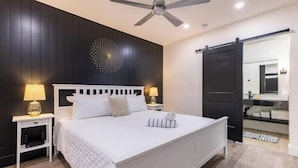 Een moderne slaapkamer met een groot bed, twee nachtkastjes met lampen, een plafondventilator en een donkere houten wand met een decoratieve verlichtingsarmatuur.