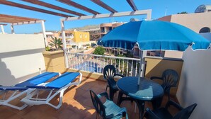 A balcony with blue lounge chairs, a table, and a blue umbrella.