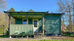 A small, single-story building with a porch and a door, surrounded by trees and grass. - 1 bedroom cozy home in Färjestaden (Färjestaden)