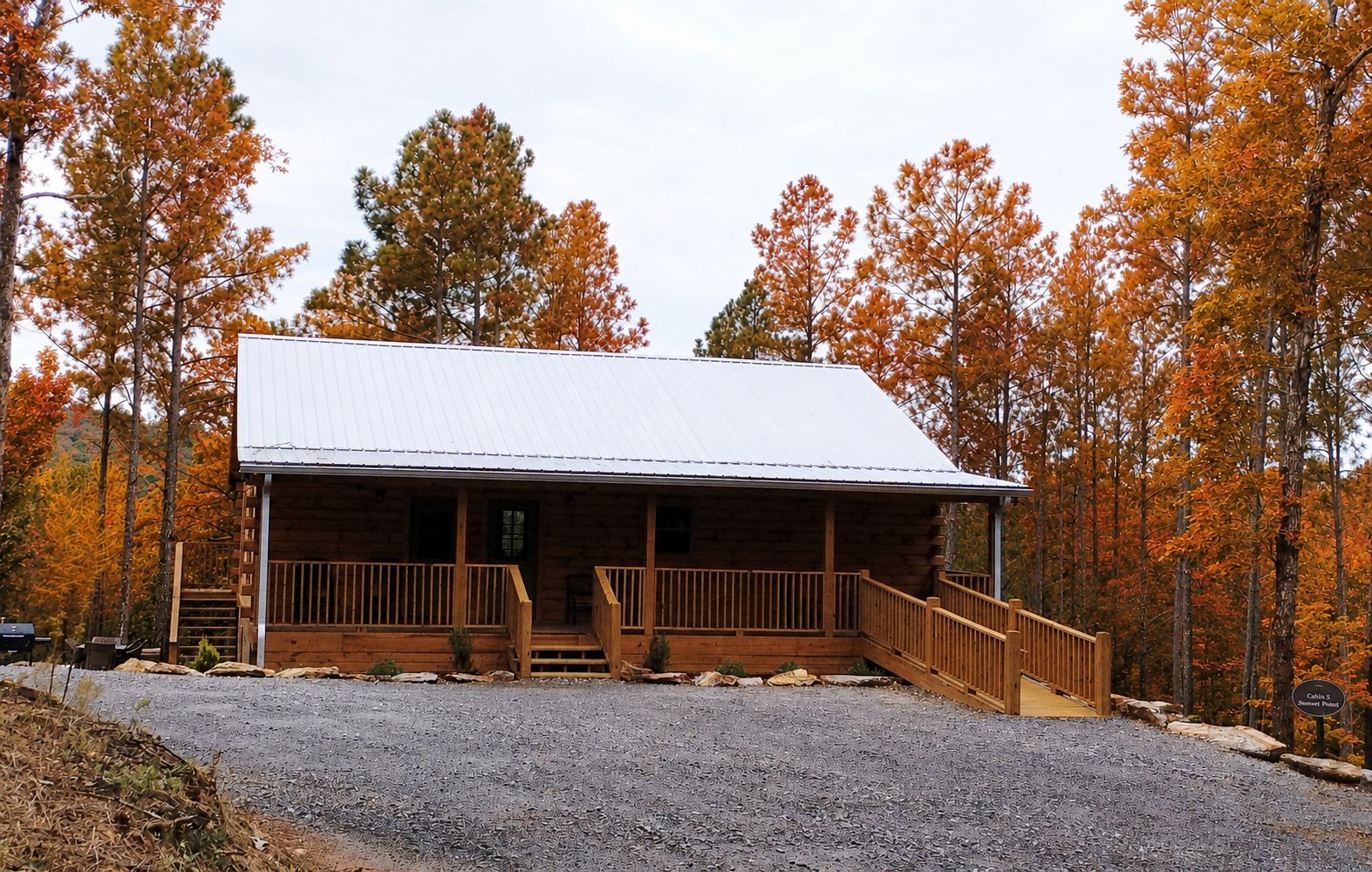 A log cabin with a porch and a metal roof, surrounded by autumn-colored trees.
