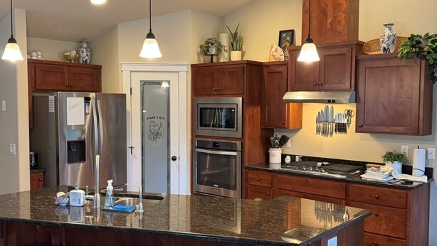 A modern kitchen with a large island, bar stools, stainless steel appliances, wooden cabinets, and pendant lighting.