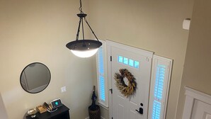 A staircase with white railings leading to a landing with a white door, a mirror, a black console table, and a hanging light fixture.
