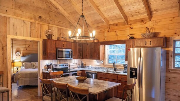 Una cocina acogedora de estilo rústico con paredes de madera, una isla central con taburetes, un refrigerador de acero inoxidable y un microondas sobre la estufa.