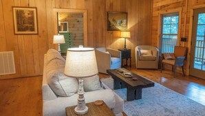 Interior acogedor de una cabaña de madera con un sofá, sillones, una lámpara y cuadros enmarcados en las paredes.