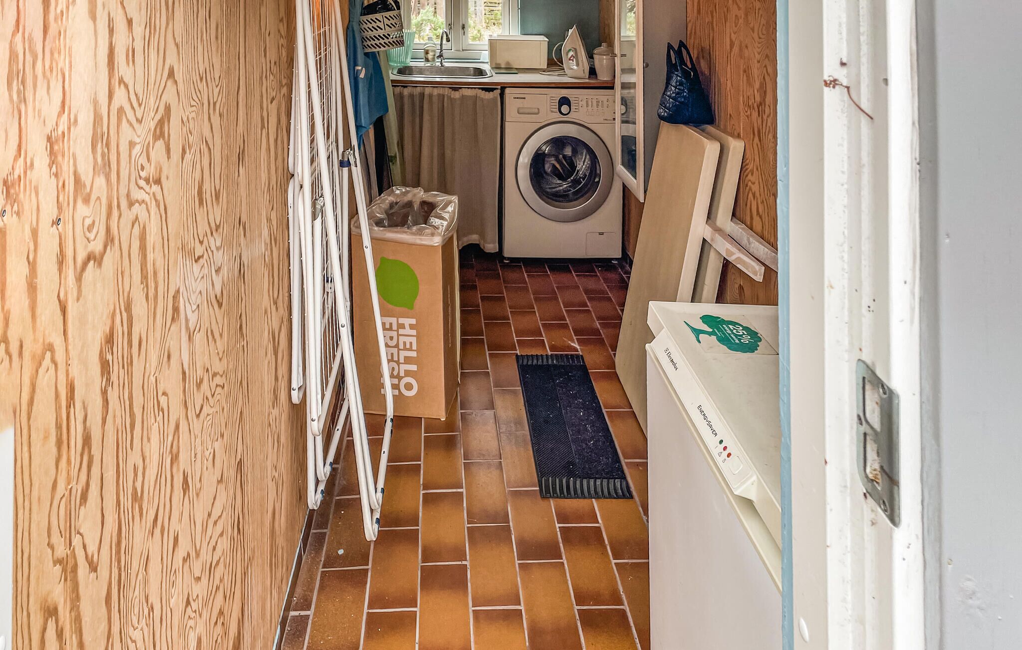 A laundry area with a washing machine, a drying rack, and a trash bin.