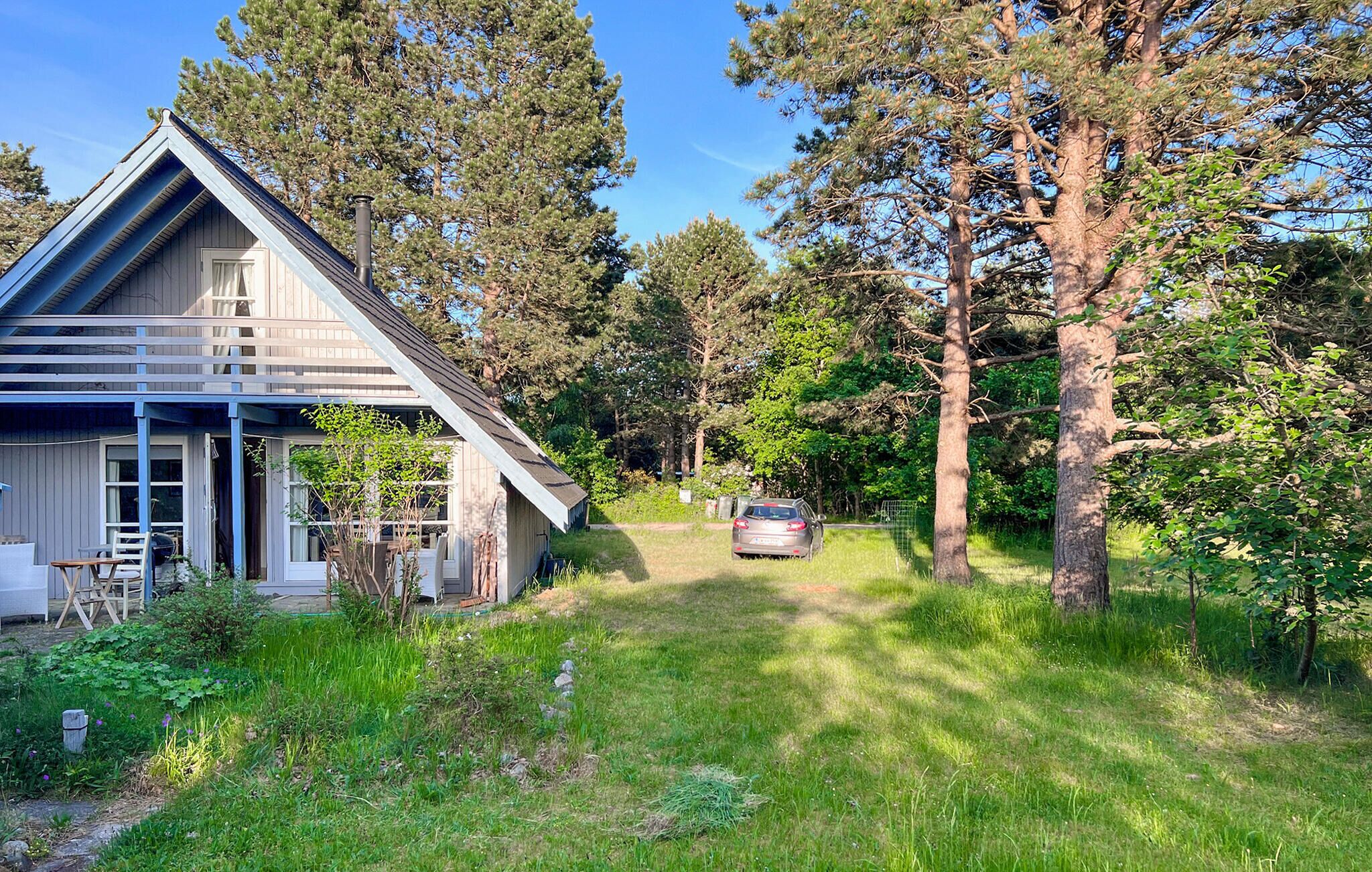 Una casa con portico, un'auto parcheggiata nel vialetto e una zona boschiva circostante.