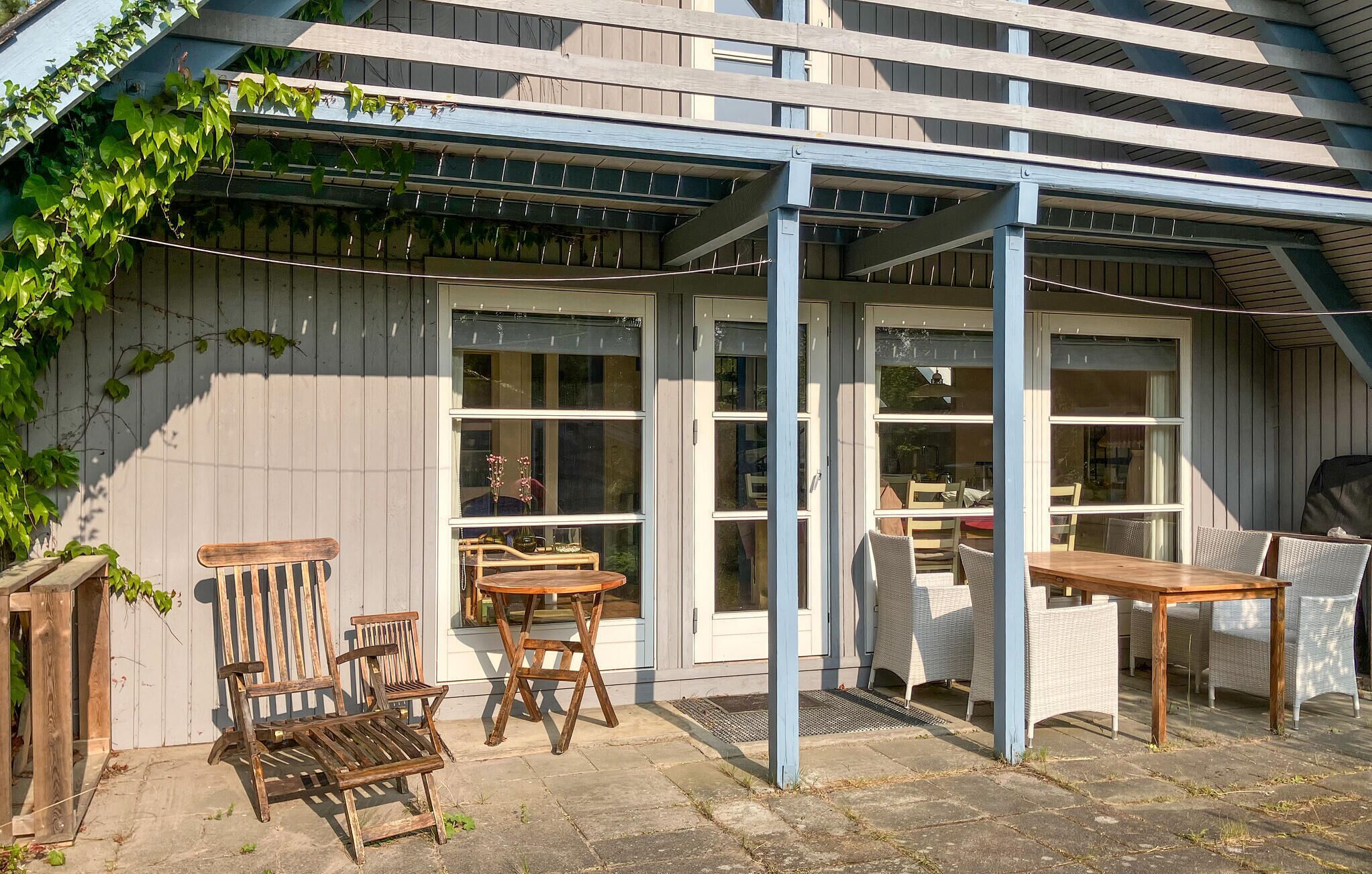 An outdoor patio with wooden furniture, a pergola, and a view of the interior through large windows.