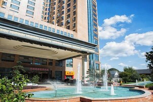 Un hotel con una fuente, un acceso cubierto y un edificio grande al fondo.
