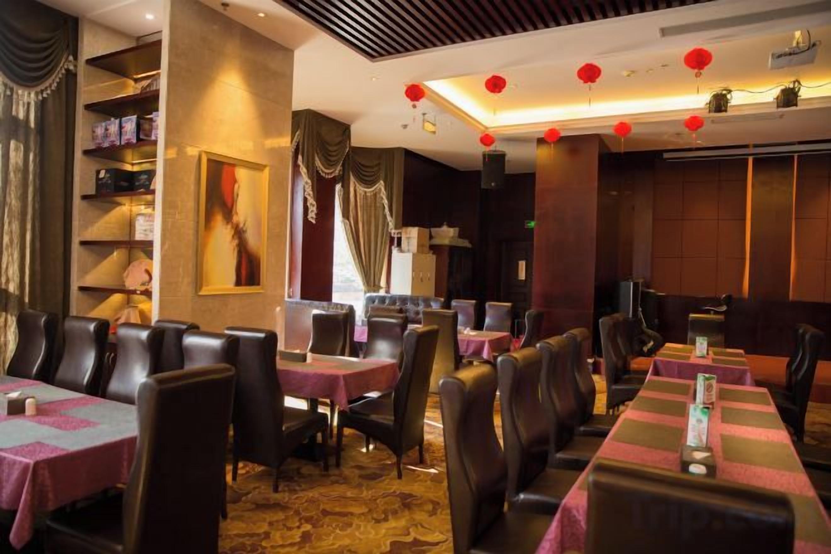 Un restaurant avec de nombreuses tables et chaises, une moquette à motifs et des lanternes rouges suspendues au plafond.