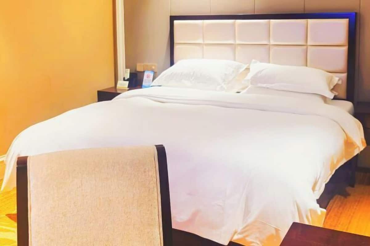 A neatly made bed with white linens and a headboard with a padded design.