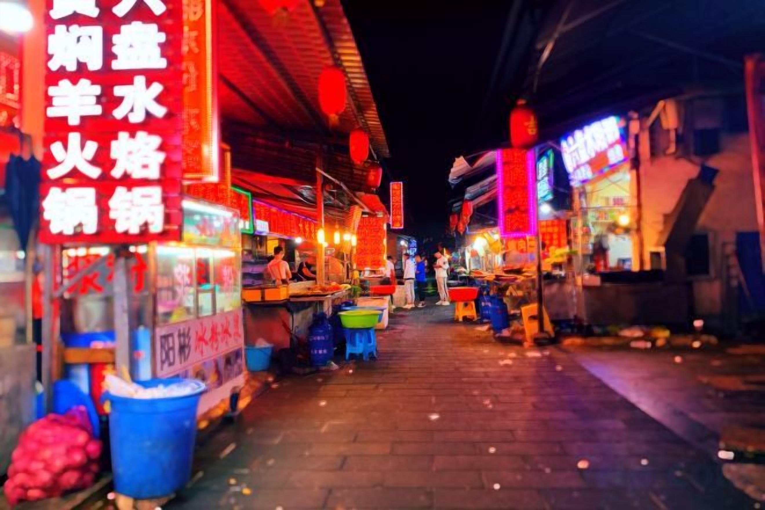 Una escena nocturna en la calle con puestos de comida y letreros de neón.