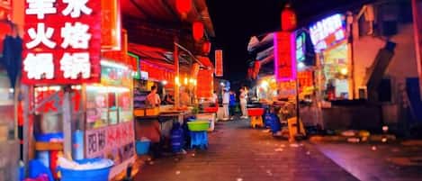 A nighttime street scene with food stalls and neon signs.