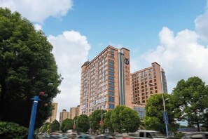 A multi-story building with a prominent clock tower, surrounded by trees and other buildings. - Puhua Hotel (Anshun)