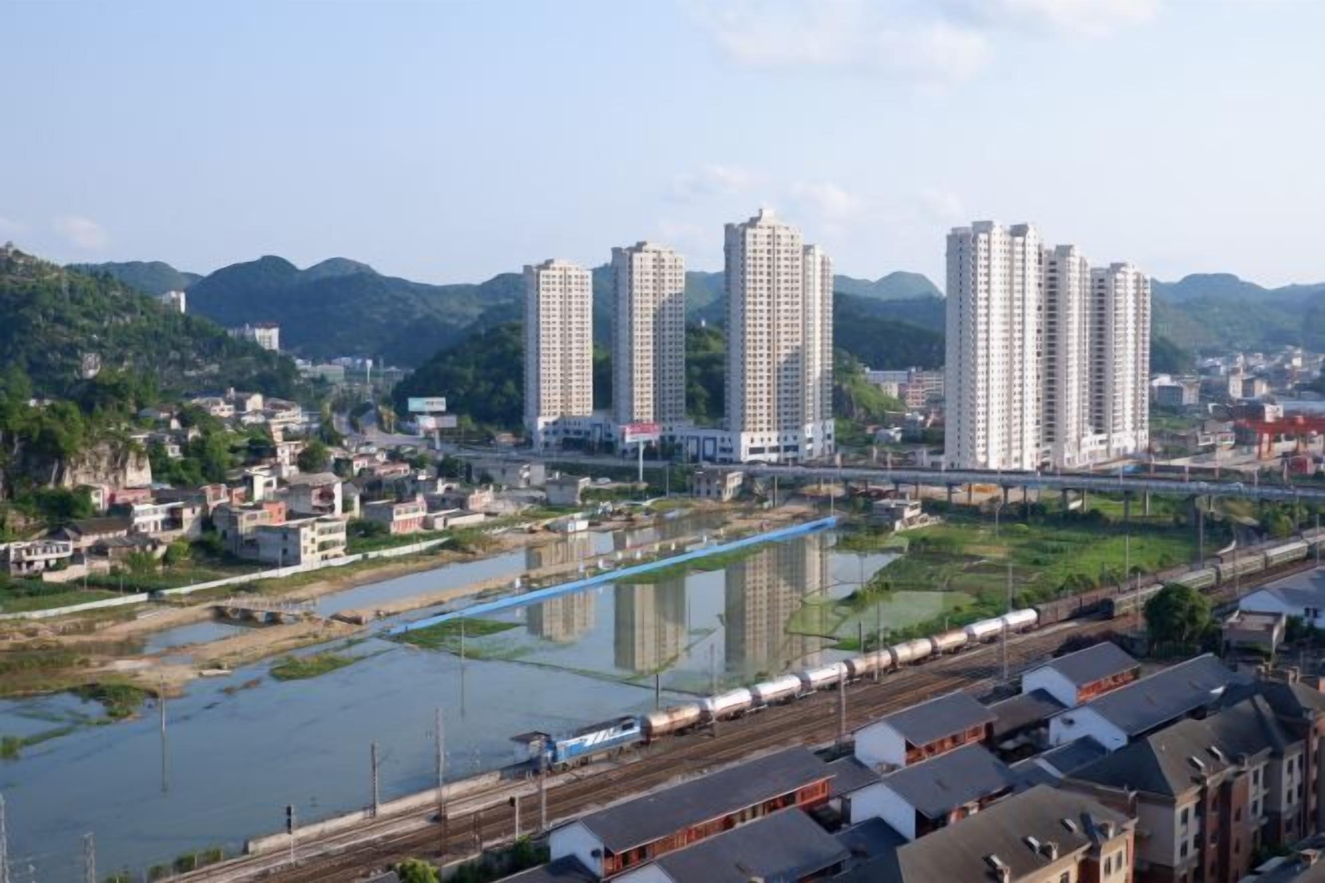 A river with a train passing, surrounded by residential buildings and a bridge.